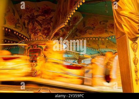 Rock 'n' Roll Waltzer in Aktion. Rasante, verschwommene Fahrt auf dem Gelände mit farbenfrohen Details des bunt bemalten Vintage-Dachs und der Beleuchtung. Stockfoto