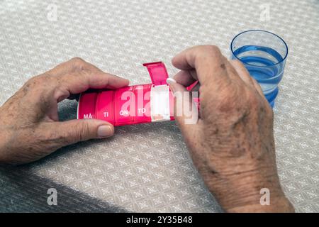Großaufnahme der weiblichen älteren Hand, die Medizin aus der medizinischen Pille Box nimmt, Sortieren Pillen. Die tägliche Dosis des Arzneimittels für eine Woche wird in eine wöchentliche Dose gegeben Stockfoto