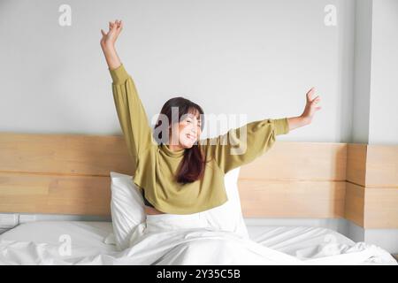 Porträt der Schönheit glückliche asiatische Frau, die aufwacht auf dem Bett (Schlaf). Junge, schöne asiatische Mädchen, die ihre Arme in den frühen Morgenstunden streckt, entspann dich Stockfoto