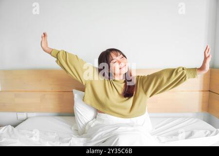 Porträt der Schönheit glückliche asiatische Frau, die aufwacht auf dem Bett (Schlaf). Junge, schöne asiatische Mädchen, die ihre Arme in den frühen Morgenstunden streckt, entspann dich Stockfoto