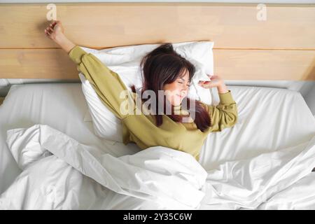 Porträt der Schönheit glückliche asiatische Frau, die aufwacht auf dem Bett (Schlaf). Junge, schöne asiatische Mädchen, die ihre Arme in den frühen Morgenstunden streckt, entspann dich Stockfoto