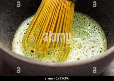 Frisch zubereiteter Bio-Matcha-Grüntee in einer Schüssel mit einem Bambusquirl. Traditionelle japanische Getränkezeremonie. Makroaufnahme Stockfoto