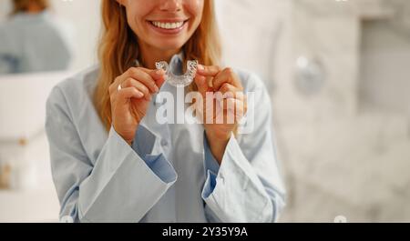 Eine fröhliche und lächelnde Frau hält in ihrem hellen Badezimmer klare Zahnausrichtungen Stockfoto
