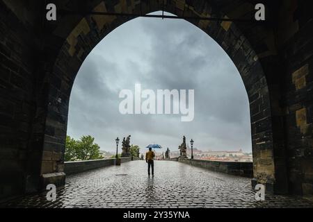 Einsamer Mann mit Schirm in der Altstadt im Regen. Rückansicht einer Person, die an düsteren Tagen durch das antike Tor zur Karlsbrücke in Prag spaziert. Stockfoto