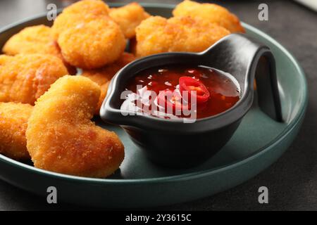 Teller mit heißer Chili-Sauce und Nuggets auf grauem Tisch, Nahaufnahme Stockfoto