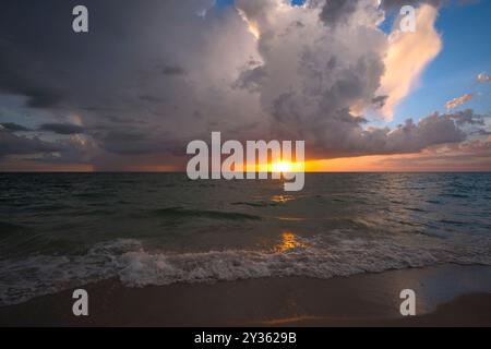 Regenwolken über rauem Seewasser. Abendliche Meereswellen brechen am Sandstrand. Wunderschöne Meereslandschaft bei Sonnenuntergang Stockfoto