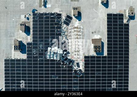 Draufsicht der durch den Hurrikan Ian zerstörten Photovoltaik-Solarpaneele, die auf dem Dach des Industriebaues zur Erzeugung von ökologischem Strom montiert sind Stockfoto
