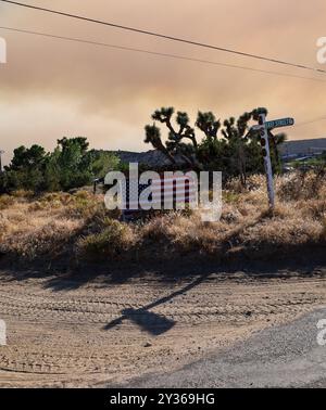 Phelan, Kalifornien, USA. September 2024. Rauch erfüllt den Himmel dahinter, während eine amerikanische Flagge auf der Easy Street sitzt, während das Bridge Fire in der Nähe der Straße nach Wrightwood, Highway 138 und dem Pear Blossom Highway zwischen Llano und Phelan, Kalifornien, brennt. (Kreditbild: © Amy Katz/ZUMA Press Wire) NUR REDAKTIONELLE VERWENDUNG! Nicht für kommerzielle ZWECKE! Stockfoto