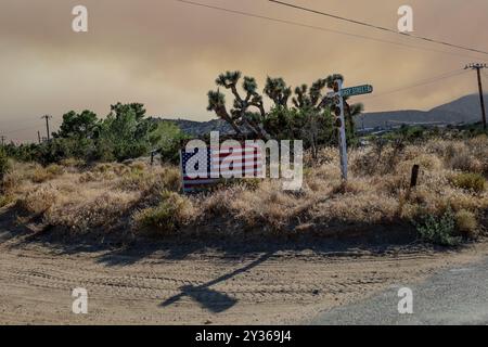 Phelan, Kalifornien, USA. September 2024. Rauch erfüllt den Himmel dahinter, während eine amerikanische Flagge auf der Easy Street sitzt, während das Bridge Fire in der Nähe der Straße nach Wrightwood, Highway 138 und dem Pear Blossom Highway zwischen Llano und Phelan, Kalifornien, brennt. (Kreditbild: © Amy Katz/ZUMA Press Wire) NUR REDAKTIONELLE VERWENDUNG! Nicht für kommerzielle ZWECKE! Stockfoto