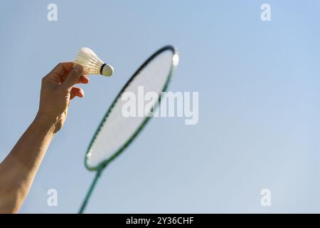 Weißer Badminton-Shuttlecock und Badminton-Schläger in Menschenhand gegen klaren blauen Himmel. Sommerspiel. Outdoor-Aktivitäten. Kopierbereich. Stockfoto