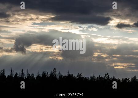 Ein dramatischer Himmel mit dunklen Wolken und Sonnenstrahlen, die durchbrechen und die Landschaft darunter beleuchten. Silhouetten säumen den Horizont und schaffen Stockfoto