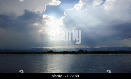 Sonnenlicht durchdringt Wolken und beleuchtet einen ruhigen See in Myanmar Stockfoto