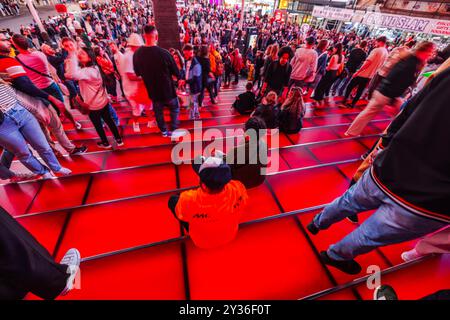 Wunderschöner Blick auf die überfüllten roten Stufen am Times Square, New York, mit Menschen, die zu Fuß und im Sitzen gehen und die pulsierende Energie der Stadt bei Nacht einfangen. Neu Stockfoto