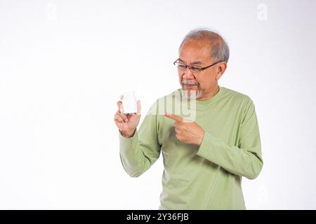 Porträt asiatischer älterer Mann mit Brille zeigt auf ein weißes Pillenflaschenstudio, isoliert auf weiß Stockfoto