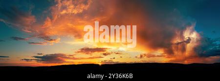 Dramatische Sturmwolken, die bei Sonnenuntergang in leuchtendem Orange und Gelb leuchten. Eine Panoramaaufnahme eines Wetterphänomens. Stockfoto