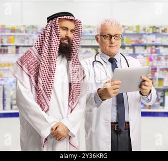 Ein Arzt und ein saudi-arabischer Mann, der sich ein digitales Tablet in einer Apotheke ansieht Stockfoto