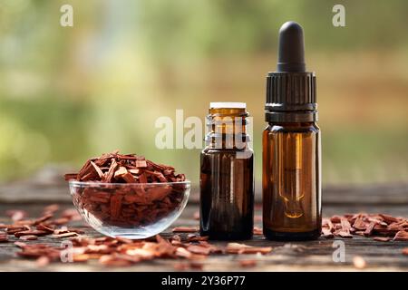 Zwei braune Flaschen ätherisches Aromatherapie-Öl mit roten Sandelholzchips in einer Schüssel im Freien in der Natur Stockfoto