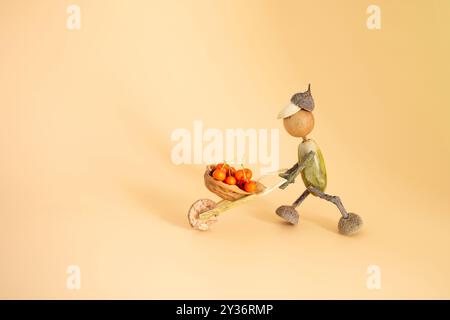 Handgefertigte herbstliche Figur aus Eicheln, Schubkarre mit Beerenfüllung, DIY-Konzeptkunst, Aktivitäten für Kinder, Natur inspirierte Dekoration, Herbst cr Stockfoto
