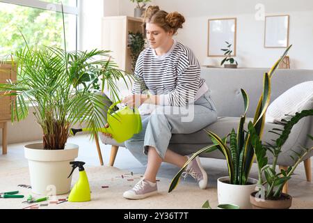 Junge Frau, die zu Hause grüne Pflanzen bewässert Stockfoto