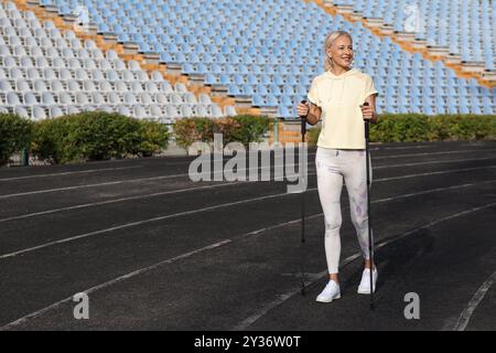 Schöne reife glückliche Frau, die mit Gehstöcken im Stadion trainiert Stockfoto