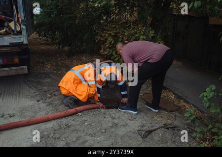 Kanalisationsarbeiter, die den Gullyschacht reinigen und die Kanalisation auf der Straße freimachen. Stockfoto