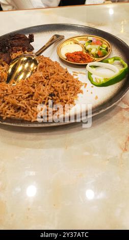 45°-Porträt von Nasi Kebuli (Kebuli-Reis) in der Mitte mit Gurken, Sauce und Löffel, typisch arabisches Essen hergestellt in Indonesien auf dem Tisch Stockfoto