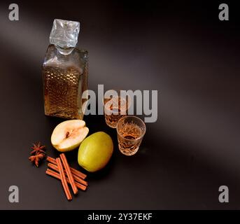 Birnenlikör mit Zimt und Anis auf schwarzem Hintergrund, hausgemachter starker Alkohol mit Gewürzen in einer Kristallschale. Nahaufnahme. Stockfoto