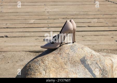 Ein Paar beige Absätze, die auf einem Felsen in der Nähe einer Holzbrücke sitzen Stockfoto