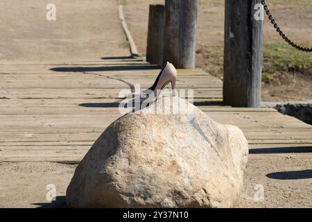 Ein Paar beige Absätze, die auf einem Felsen in der Nähe einer Holzbrücke sitzen Stockfoto