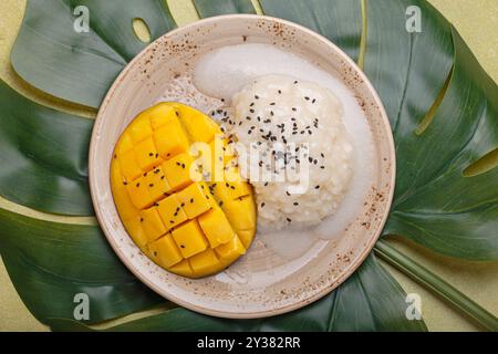 Traditionelles Dessert von Thailand, köstlicher Mango-Kleberreis mit Kokosnussmilch und Sesamsamen auf tropischem Blatt von oben Stockfoto