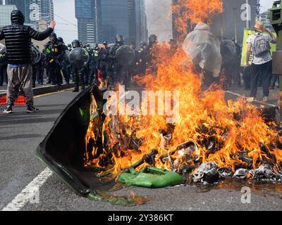 Das Victoria Police Response Team für öffentliche Ordnung wird durch die Flammen eines Müllfeuers von Demonstranten gesehen. Eine geplante Blockade und Protest der Land Forces 2024, die größte Ausstellung der Verteidigungsindustrie in der südlichen Hemisphäre, brach den ganzen Tag über in Auseinandersetzungen mit der Polizei aus. Die Demonstranten, die versuchten, den Zugang zum Kongress zu verhindern, warfen Gegenstände und Flüssigkeiten auf Offiziere, bauten kleine Blockaden und begannen Müllfeuer, während die Polizei Gewalt, Pfefferspray, Tränengas, Betäubungsgranaten und Gummigeschosse auf die Demonstranten einsetzte Stockfoto