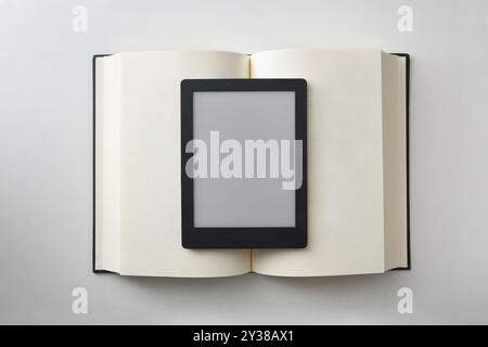 Vergleich zwischen digitalem Lesen und Papier mit eBook auf offenem Papierbuch isoliert auf weißem Tisch. Draufsicht Stockfoto