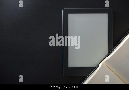Detail des E-Books auf einem schwarzen Tisch mit offenem, traditionellem Papierbuch. Lesekonzept im elektronischen Buch. Draufsicht Stockfoto