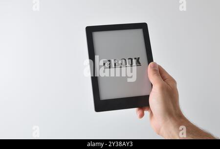 Detail der Hand, die ein eBook mit geschriebenem Text auf weißem Hintergrund nimmt. Vorderansicht Stockfoto