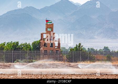 Israel und Jordanien Staatsgrenze. Wachturm mit Jordan-Flagge in Aqaba, Jordanien. Landwirtschaftliche Felder mit Bewässerungssystem in Eilat, Israel Stockfoto