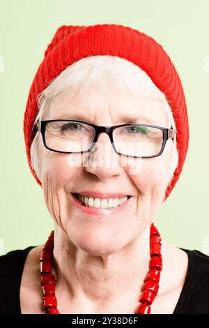 Mode, Brille und Porträt einer alten Frau im Studio mit stilvollem, trendigem Accessoire und Winterkleidung. Glücklich, lächeln und Gesicht einer isolierten Person mit Stockfoto