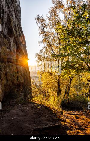 Wenn die Sonne untergeht, leuchtet goldenes Licht durch die Sandsteinfelsen, das warme Farbtöne auf die umliegenden Bäume wirft und die lebhaften Farben des Herbstes in einer ruhigen Landschaft zeigt. Stockfoto