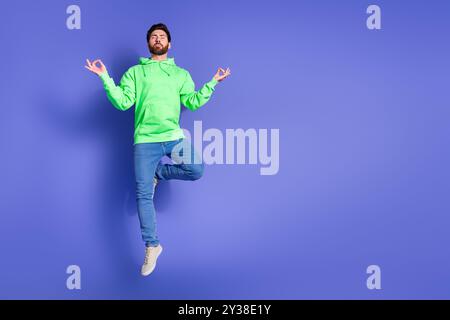 Ganzkörperfoto des attraktiven jungen Mannes Sprung Meditation gekleidet stilvolle grüne Kleidung isoliert auf violettem Hintergrund Stockfoto