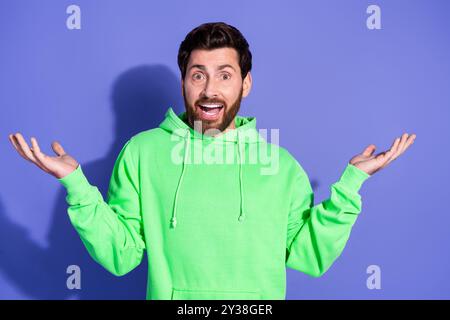 Foto-Porträt des gutaussehenden reiferen Alters funky Mann trägt hellgrünen Hoodie Sportswear verwirrte zuckte Schultern isoliert auf violettem Hintergrund Stockfoto