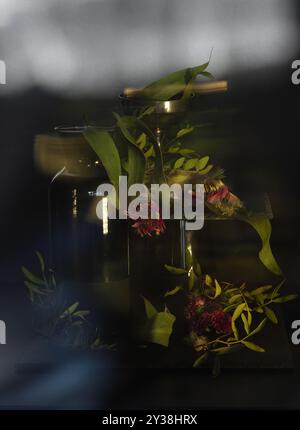Ein Stillleben mit verwelkten Blumen in einer schwarzen Vase und Glas. Getrocknete Blätter auf dunklem Hintergrund bringen ein Element der Zeit und des Verfalls ins Bild Stockfoto