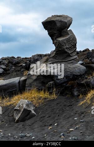 Ein großer Felsen liegt auf einem felsigen Hügel. Vulkanisches Gelände. Der Himmel ist bewölkt und der Felsen ist von einem Grasfeld umgeben Stockfoto