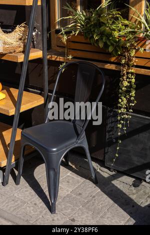 Ein schwarzer Metallstuhl neben Holzregalen und Pflanzen in einer sonnigen Umgebung im Freien Stockfoto