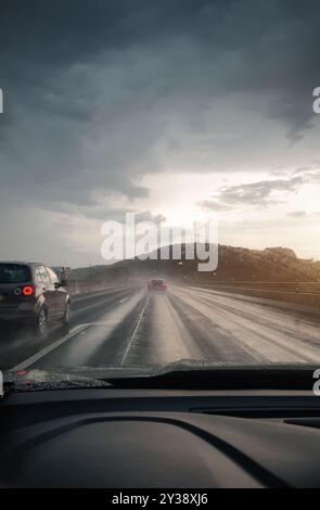 Bei Regen auf der Autobahn fahren. Schwindender perspektivischer Blick auf das Autofahren auf der deutschen Autobahn bei Sonnenuntergang. Stockfoto