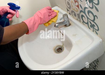 Hände in rosafarbenen Gummihandschuhen desinfizieren ein Waschbecken im Badezimmer mit Spray und Tuch. Stockfoto