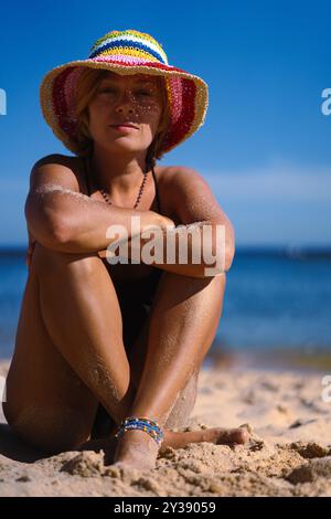 Eine Frau in Badeanzug und mehrfarbigem Hut liegt am Strand. Stockfoto