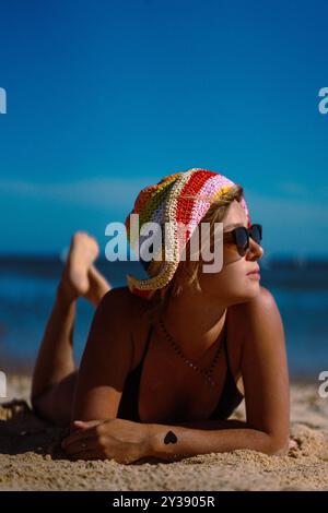 Eine Frau in Badeanzug und mehrfarbigem Hut liegt am Strand. Stockfoto