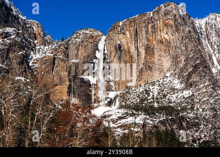 Ribbon Falls im Winter umgeben von schneebedeckten Klippen und strahlend blauem Himmel. Stockfoto