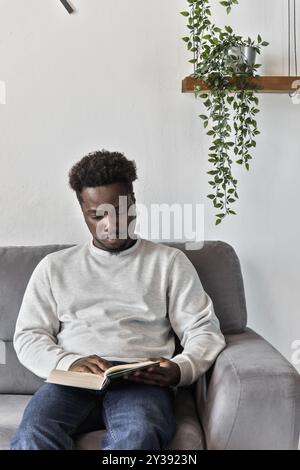 Ein Afroamerikaner liest Buch und sitzt allein auf der Couch Stockfoto