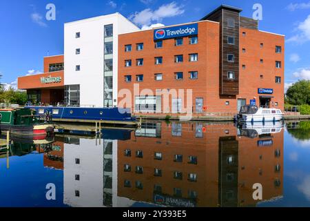 Grand Union Canal im Aylesbury Basin, der den Supermarkt Waitrose, das Travelodge Hotel, die Lastkähne und das Motorboot widerspiegelt. Mit stillen Gewässern und blauem Himmel. Stockfoto