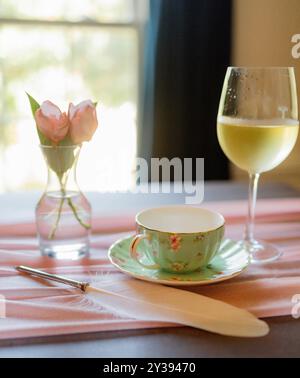 Porzellan-Teetasse und ein Glas Wein auf einem pastellfarbenen Tisch Stockfoto